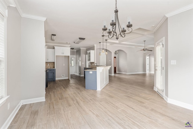 kitchen with arched walkways, baseboards, white cabinets, ceiling fan with notable chandelier, and open floor plan