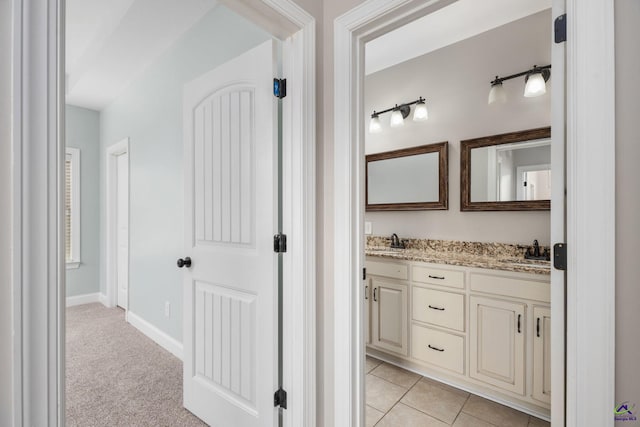 full bath with baseboards, double vanity, a sink, and tile patterned flooring