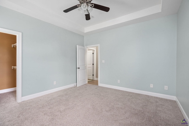 empty room featuring a raised ceiling, ceiling fan, and carpet