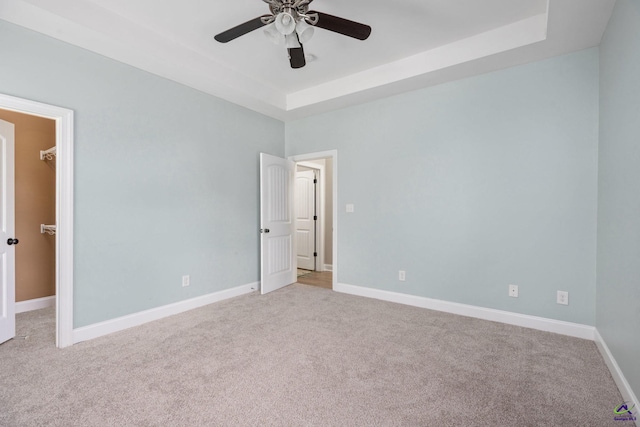 spare room with a raised ceiling, ceiling fan, and light carpet