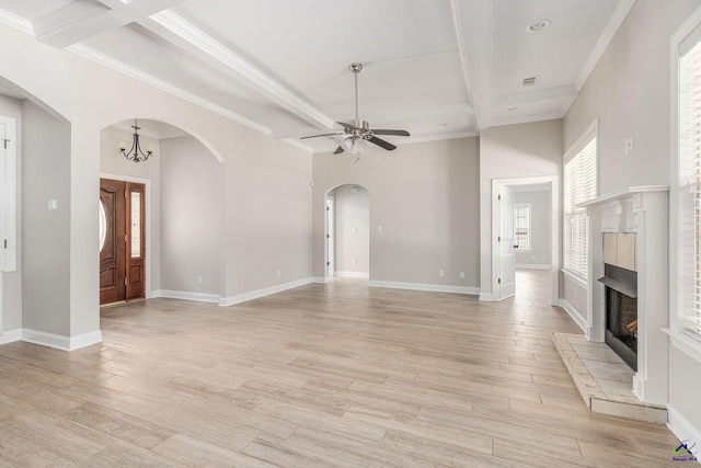 unfurnished living room featuring beamed ceiling, light wood-style floors, a warm lit fireplace, arched walkways, and ceiling fan with notable chandelier