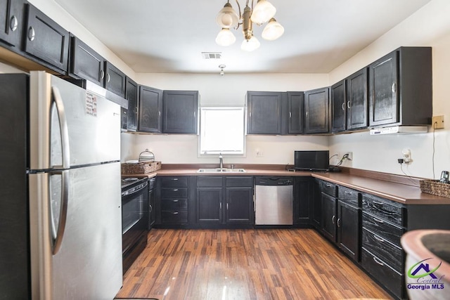 kitchen featuring dark countertops, dark wood-style floors, a chandelier, a sink, and appliances with stainless steel finishes