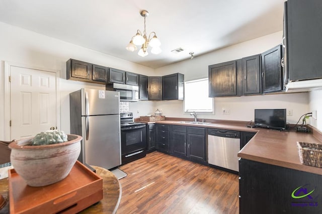 kitchen featuring decorative light fixtures, wood finished floors, a sink, an inviting chandelier, and stainless steel appliances