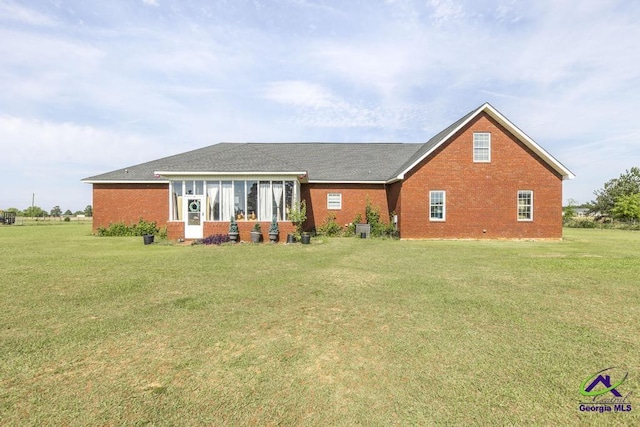 rear view of house with a shingled roof, a yard, and brick siding