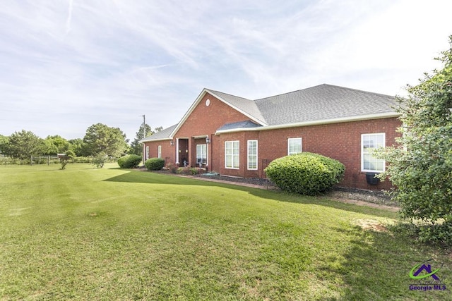 view of front of property with roof with shingles, a front lawn, and brick siding