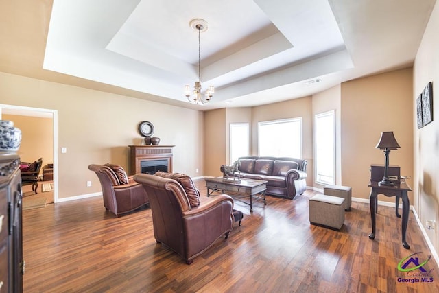 living room with a raised ceiling, baseboards, dark wood-style floors, and a notable chandelier