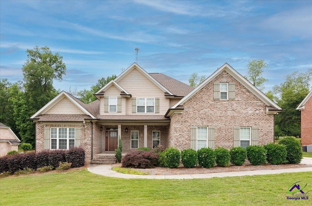 craftsman house featuring a front lawn, a shingled roof, brick siding, and covered porch