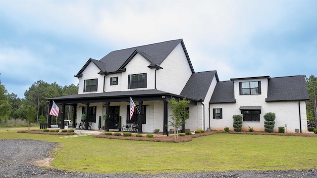modern farmhouse style home featuring covered porch, roof with shingles, brick siding, and a front yard