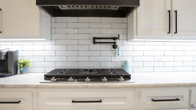 interior details with extractor fan, stainless steel gas stovetop, backsplash, and white cabinets