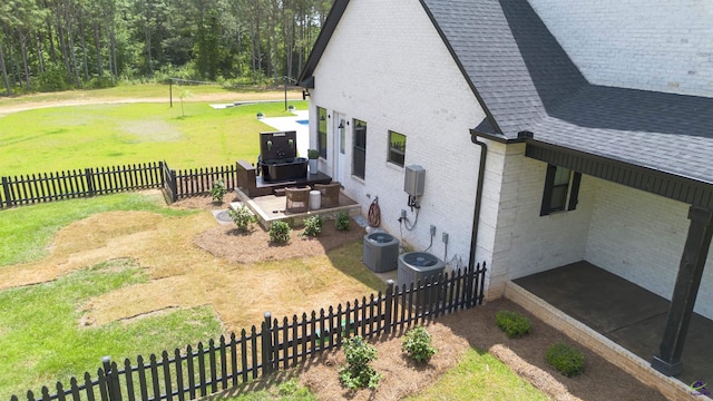 view of side of home with central air condition unit, brick siding, a yard, a fenced backyard, and a shingled roof
