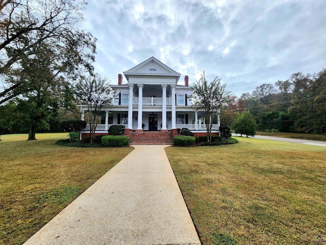 greek revival house with a balcony, a front yard, a chimney, and covered porch