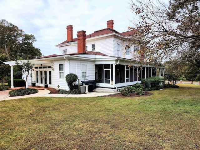 rear view of property with a yard, a sunroom, french doors, and a chimney