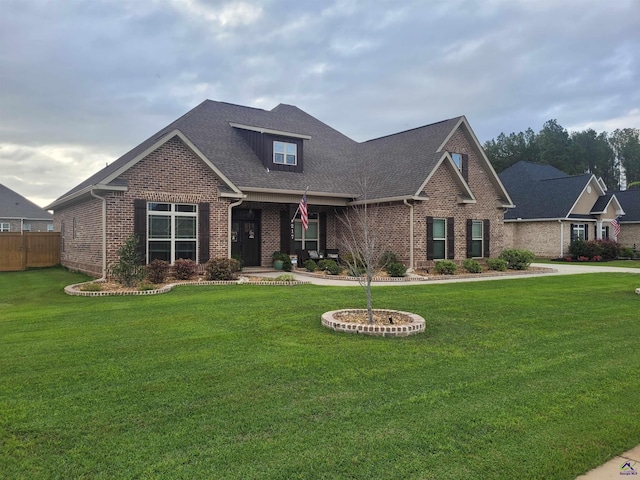 craftsman-style house with a shingled roof, brick siding, fence, and a front yard