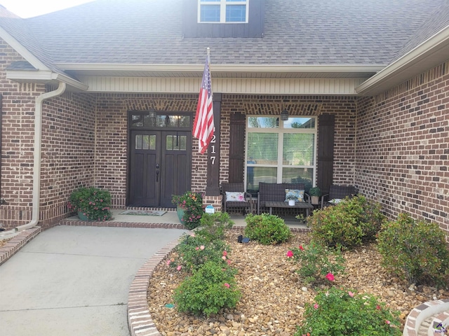 entrance to property featuring roof with shingles, a porch, and brick siding