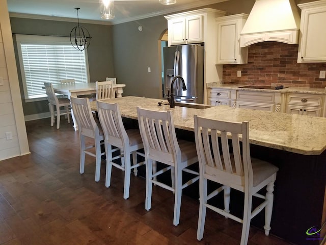 kitchen featuring custom exhaust hood, a sink, stainless steel fridge, arched walkways, and black electric stovetop