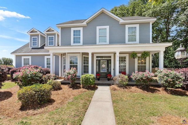 view of front facade with a front yard, a shingled roof, and covered porch