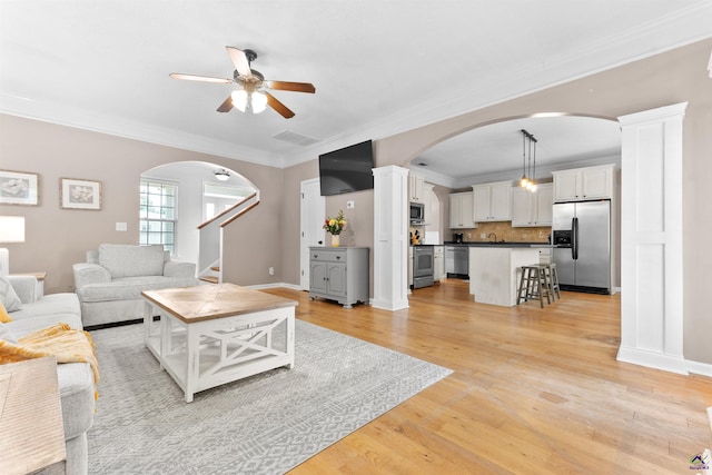 living room with stairs, ornamental molding, light wood-type flooring, arched walkways, and a ceiling fan