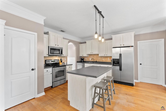 kitchen with a sink, stainless steel appliances, ornamental molding, arched walkways, and dark countertops