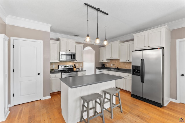 kitchen with a sink, dark countertops, crown molding, appliances with stainless steel finishes, and tasteful backsplash