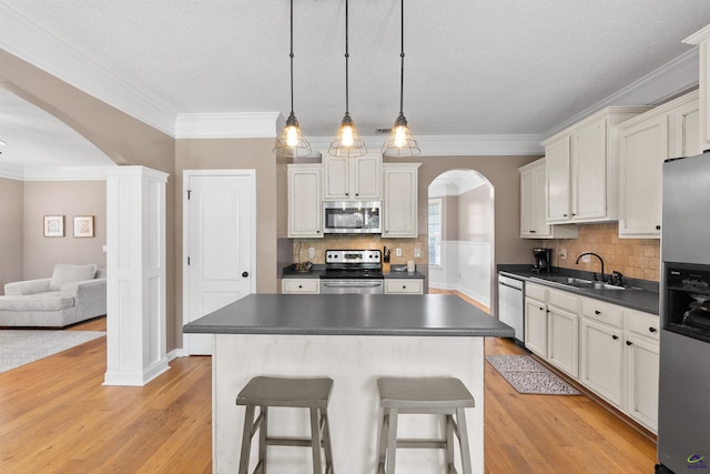 kitchen featuring a sink, arched walkways, dark countertops, stainless steel appliances, and light wood-type flooring