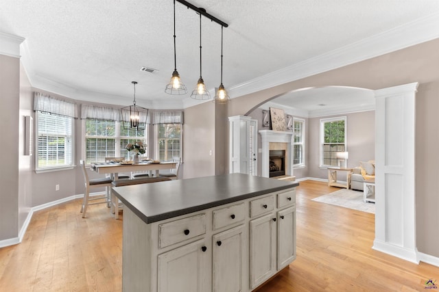 kitchen featuring arched walkways, dark countertops, light wood finished floors, and crown molding