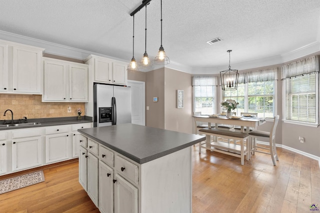 kitchen with a textured ceiling, visible vents, a sink, fridge with ice dispenser, and dark countertops