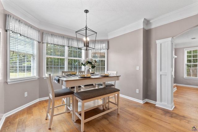 dining space featuring light wood-style flooring, baseboards, a chandelier, crown molding, and arched walkways