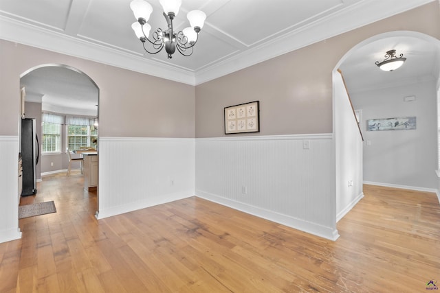 spare room with arched walkways, wainscoting, and light wood-type flooring