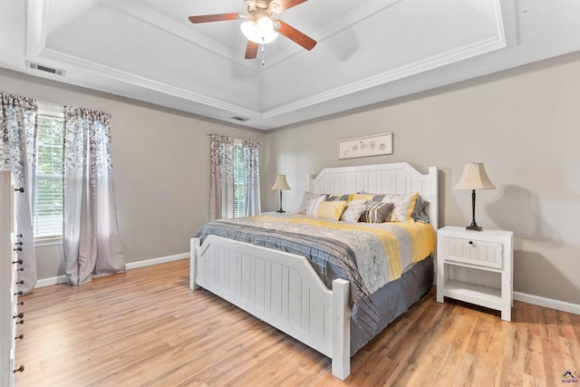bedroom featuring light wood-type flooring, visible vents, baseboards, and a raised ceiling