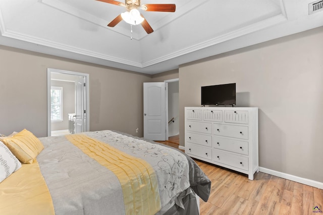 bedroom with a tray ceiling, visible vents, light wood-style flooring, and baseboards