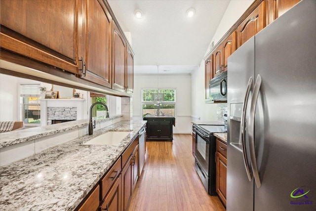 kitchen with black appliances, a sink, light wood-style floors, light stone countertops, and a stone fireplace