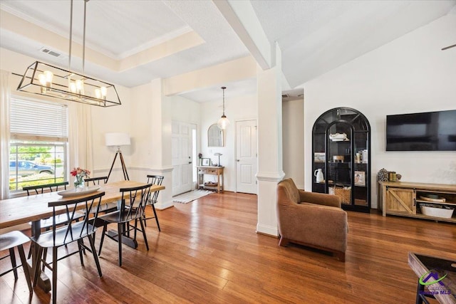 dining space featuring wood finished floors, ornate columns, a chandelier, and ornamental molding