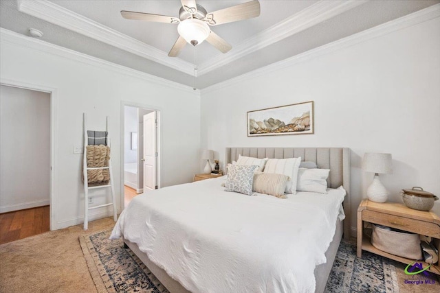 carpeted bedroom featuring crown molding, a raised ceiling, ensuite bath, ceiling fan, and baseboards