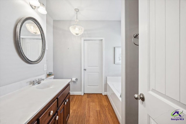 bathroom with vanity, wood finished floors, baseboards, and a bath