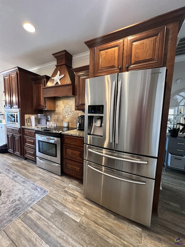 kitchen with appliances with stainless steel finishes, tasteful backsplash, light stone counters, custom exhaust hood, and light wood finished floors