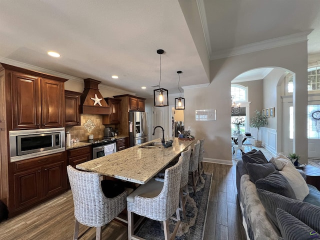 kitchen featuring custom range hood, appliances with stainless steel finishes, a sink, arched walkways, and open floor plan