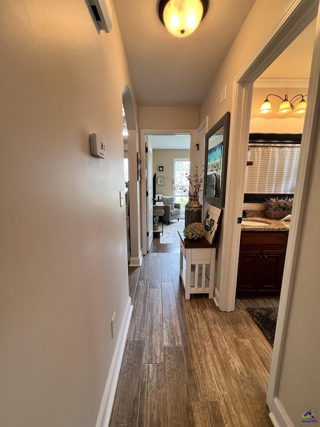 hall featuring a sink, dark wood-style flooring, and baseboards