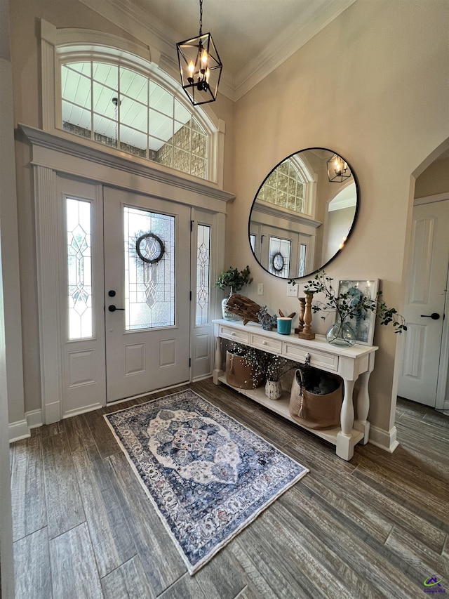 entrance foyer featuring dark wood-style floors, crown molding, baseboards, arched walkways, and a chandelier