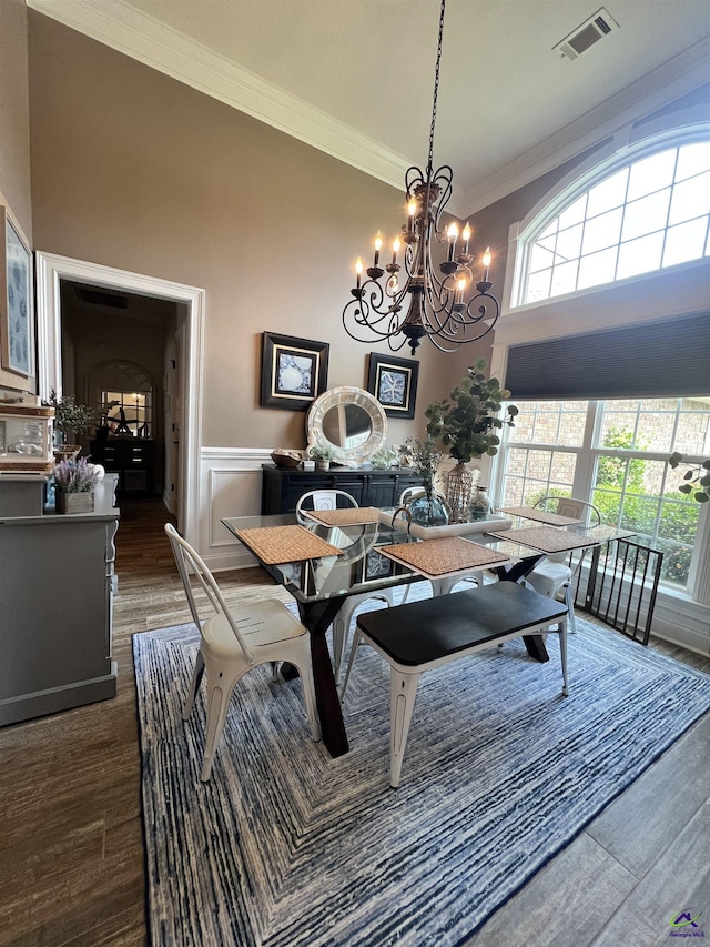 dining area with ornamental molding, a chandelier, wood finished floors, plenty of natural light, and a wainscoted wall