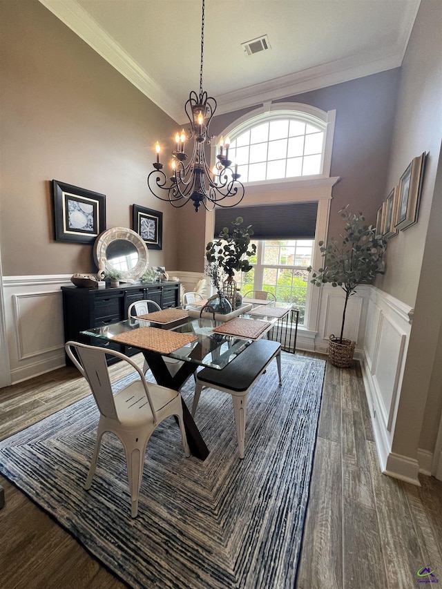 dining space with a decorative wall, crown molding, wood finished floors, a chandelier, and a wainscoted wall