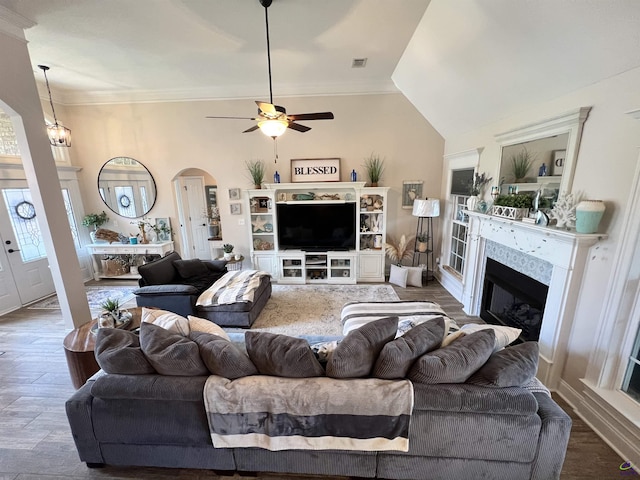living area featuring arched walkways, ceiling fan, a fireplace, crown molding, and wood finished floors