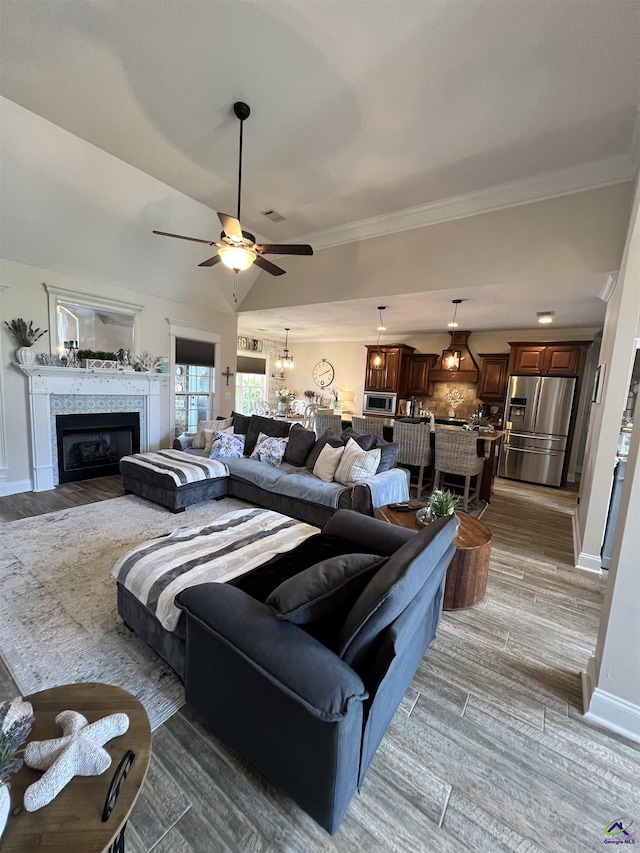 living room with a ceiling fan, baseboards, wood finished floors, a tile fireplace, and ornamental molding