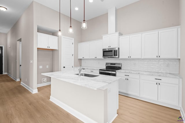 kitchen featuring appliances with stainless steel finishes, a sink, a towering ceiling, light wood-style floors, and tasteful backsplash