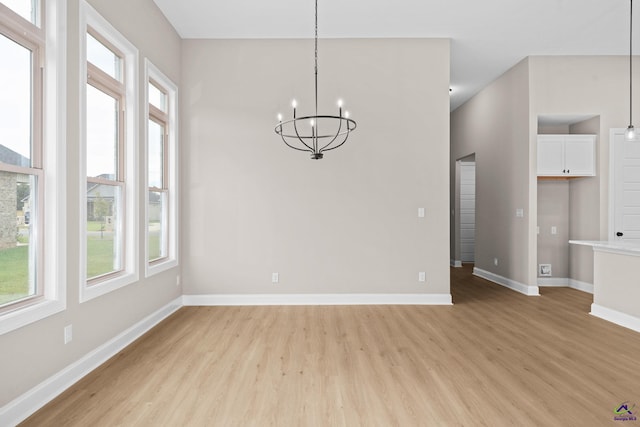unfurnished dining area featuring light wood-style floors, plenty of natural light, a chandelier, and baseboards