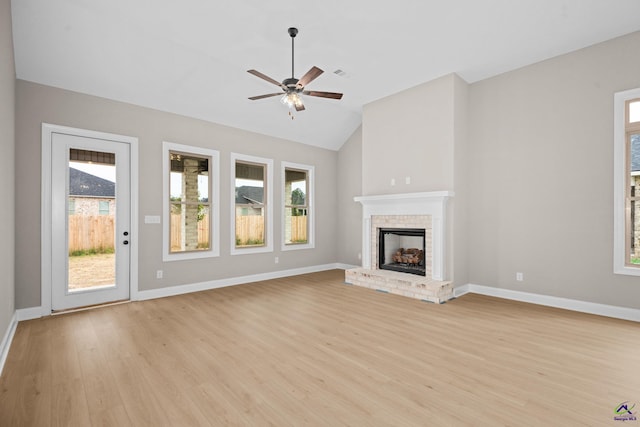 unfurnished living room with plenty of natural light, lofted ceiling, light wood finished floors, a brick fireplace, and baseboards
