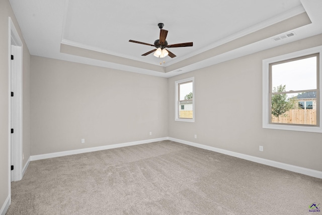 carpeted empty room featuring a raised ceiling, ornamental molding, ceiling fan, and baseboards