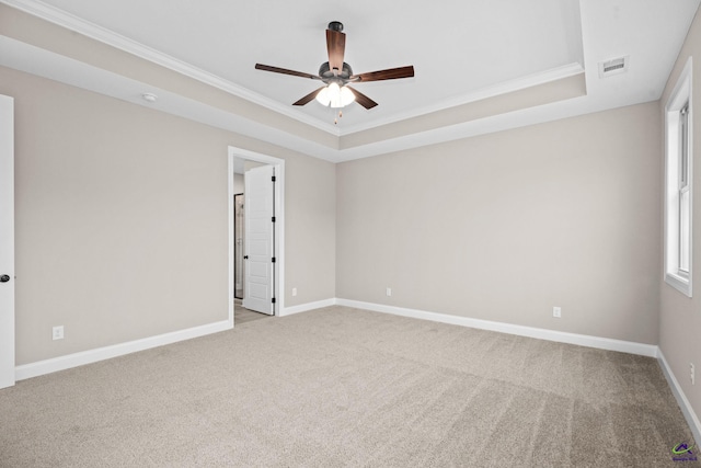 spare room featuring crown molding, light colored carpet, a ceiling fan, a tray ceiling, and baseboards