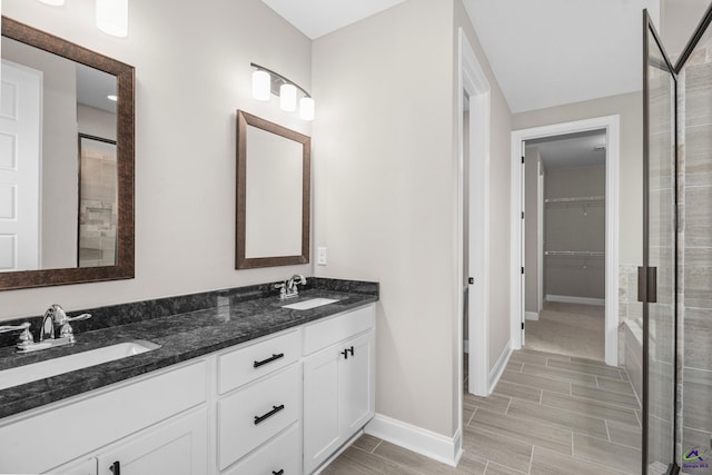 bathroom featuring baseboards, a spacious closet, wood tiled floors, double vanity, and a shower