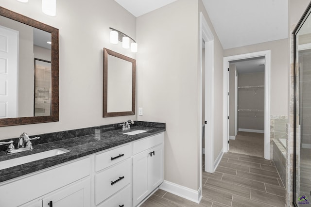 full bath featuring baseboards, wood tiled floors, a spacious closet, double vanity, and tiled shower
