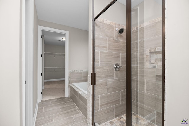 bathroom with a stall shower, tiled bath, baseboards, and a walk in closet